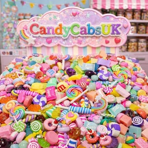 Op de afbeelding: Een kleurrijke verzameling snoep, waaronder lolly's, harde snoepjes en chocolade. De snoepjes zijn op een hoop gerangschikt, met een bord met de tekst "CandyCabsUK" in een wolk-vorm. Het geheel doet denken aan een snoepwinkel.