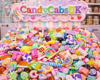 May include: A colorful display of various candies, including lollipops, hard candies, and chocolates. The candies are arranged in a pile, with a sign that reads "CandyCabsUK" in a cloud-shaped design. The overall theme is a sweet shop.