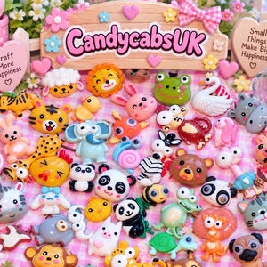 Puede incluir: Una colección de pequeños cabujones de resina coloridos y planos con varios animales de dibujos animados, incluyendo pandas, leones, ranas y elefantes. Un letrero de madera con el texto CandycabsUK y Small Things Make Big Happiness es visible.
