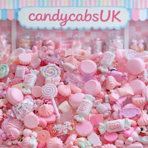 Può includere: Un grande mucchio di caramelle rosa e bianche, tra cui lecca-lecca, macarons e dolci confezionati. Il cartello sopra recita "candycabsUK". Lo sfondo presenta barattoli pieni di altre caramelle, creando un'esposizione dolce e colorata.
