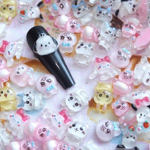 May include: A black nail with a white cartoon dog design is surrounded by an assortment of small, colorful, cartoon character nail art decorations. The decorations include bunnies, cats, and other cute figures in pink, white, and yellow.