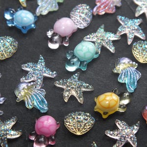 May include: Assortment of colorful, glittery, and iridescent sea-themed charms, including starfish, seashells, turtles, and jellyfish. These charms are perfect for adding a touch of whimsy to crafts, jewelry, and other projects.