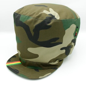 Op de afbeelding: Camouflage-stofhoed met een groene, rode en gele band rond de rand. De hoed heeft een label met de tekst "Have Faith".