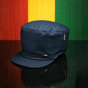 Può includere: Berretto blu navy in stile militare con visiera corta. Il berretto presenta una piccola striscia colorata e un logo sul lato. Lo sfondo presenta strisce verticali rosse, gialle e verdi.