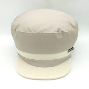 May include: A beige and white baseball cap with a white brim and a small logo on the side that says "All Made In"