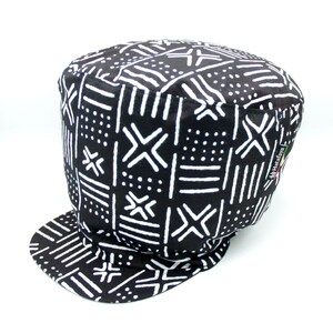 Peut inclure: Chapeau en tissu noir et blanc à bord plat. Le chapeau présente un motif géométrique avec des lignes et des points blancs sur un fond noir. Le chapeau porte une étiquette indiquant "Handwoven".