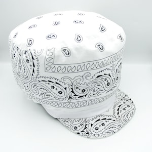 May include: White cap with a black paisley bandana print. The cap features a flat brim and a rounded crown, with the bandana pattern covering the entire surface. The design includes paisley motifs and other decorative elements.