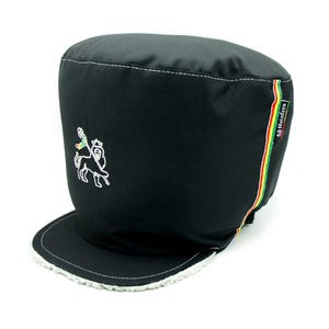 May include: Black cap with a short brim and a white embroidered lion design. The cap has a white stitched trim and a vertical stripe in red, yellow, and green. The brand name "Hatafaya" is on the side.