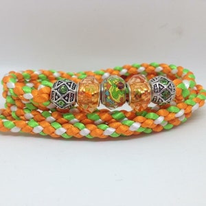 Peut inclure: Un cordon tressé avec des rayures orange, vertes et blanches. Le cordon a quatre perles dessus, une verte, une orange, une multicolore et une orange.