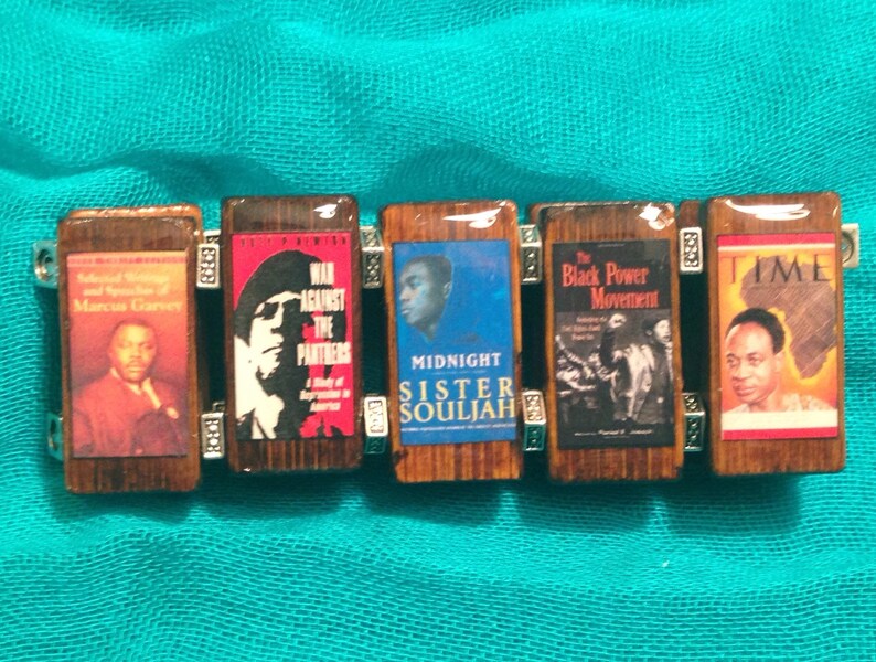 May include: A wooden bracelet with six charms featuring images of books and magazines. The charms include covers of "The Autobiography of Malcolm X", "War Against the Panthers", "Midnight Sister Souljah", "The Black Power Movement", and "Time".