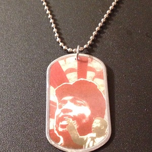 May include: A silver chain necklace with a dog tag pendant featuring a red and white image of a person singing.