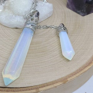 May include: Two silver and opal crystal pendants on a silver chain. The larger pendant is a long, pointed crystal with an intricate silver design. The smaller pendant is a shorter, pointed crystal with a simple silver design.