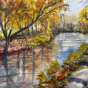 Puede incluir: Pintura a la acuarela de una escena de río con árboles en colores otoñales. El agua refleja los árboles y el cielo, creando un paisaje sereno. La obra presenta tonos de amarillo, marrón, azul y verde.