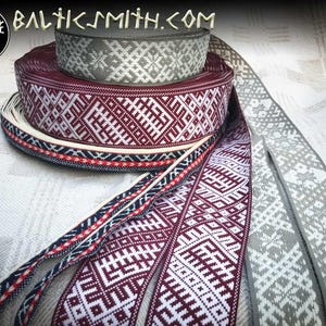 Puede incluir: Cuatro rollos de cinta de tejido tejido con intrincados patrones geométricos en tonos de gris, blanco y burdeos. La cinta se muestra sobre un fondo de tela blanca. El texto "BALTICSMITH.COM" es visible en la parte superior central de la imagen.