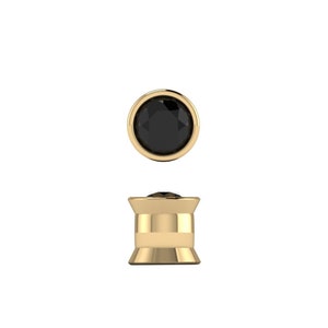 May include: A pair of gold-toned ear gauges with black gemstones. The gauges are in the shape of a cylinder with a flared base.