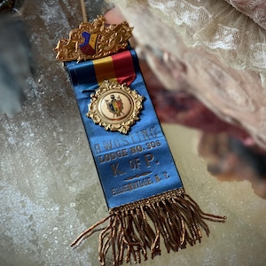 May include: A blue and gold ribbon with a gold crest and a gold medal. The ribbon has the text "Hawesling Lodge No. 208 K. of P. Elizabethville, Pa."