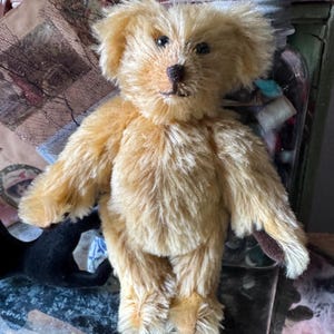 May include: A handmade, golden-brown teddy bear with a soft, plush texture. The bear has a detailed face with black eyes and a dark brown nose. Its paws and ears have darker brown accents. The bear is standing upright, showcasing its classic design.