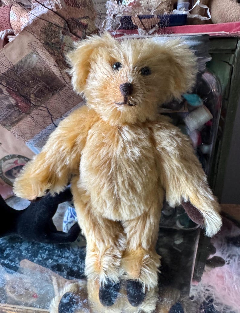 May include: A handmade, golden-brown teddy bear with a soft, plush texture. The bear has a detailed face with black eyes and a dark brown nose. Its paws and ears have darker brown accents. The bear is standing upright, showcasing its classic design.