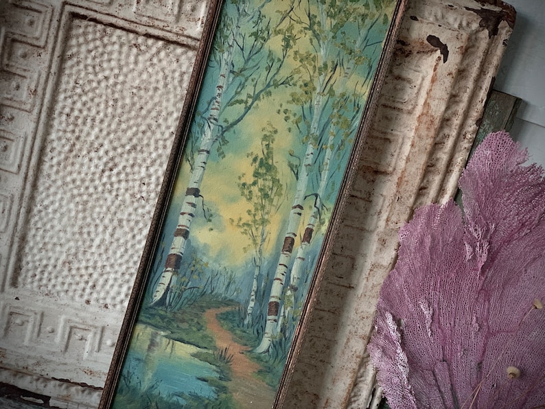Peut inclure: Une peinture encadr&eacute;e repr&eacute;sentant une sc&egrave;ne de for&ecirc;t avec trois bouleaux et un chemin menant &agrave; un petit &eacute;tang. La peinture est r&eacute;alis&eacute;e dans un style aquarelle avec des nuances de vert, de bleu et de jaune.