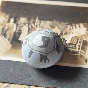 May include: A light blue egg featuring a central yin and yang symbol surrounded by a circular cracked texture pattern. The design includes dark gray markings extending outward from the center, creating a distinct contrast against the smooth surface.