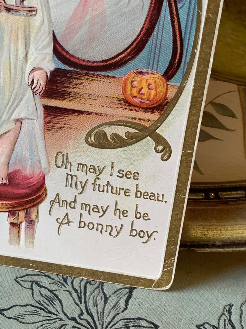 Pode incluir: Postal de Halloween vintage com borda dourada e o texto "Oh may I see My future beau, And may he be A bonny boy." A imagem apresenta uma ab&oacute;bora esculpida e uma crian&ccedil;a.