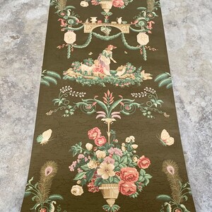May include: Vintage wallpaper roll featuring a repeating pattern of floral bouquets, a woman tending to a goat, and ornate details. The wallpaper is on a dark green background with a textured finish.