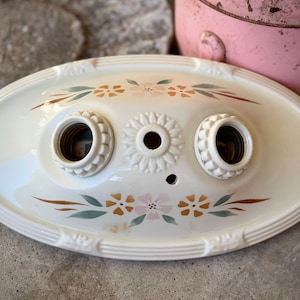 May include: White ceramic oval ceiling light fixture with two sockets and a floral design in shades of brown, green, and pink.
