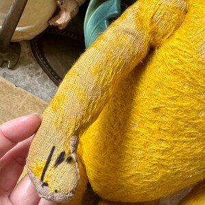 May include: Close-up of a vintage yellow teddy bear. The bear's arm is in focus, showing the textured fabric and stitching details. The bear's fur is a vibrant yellow, with a slightly worn appearance. The bear's paw has black markings.
