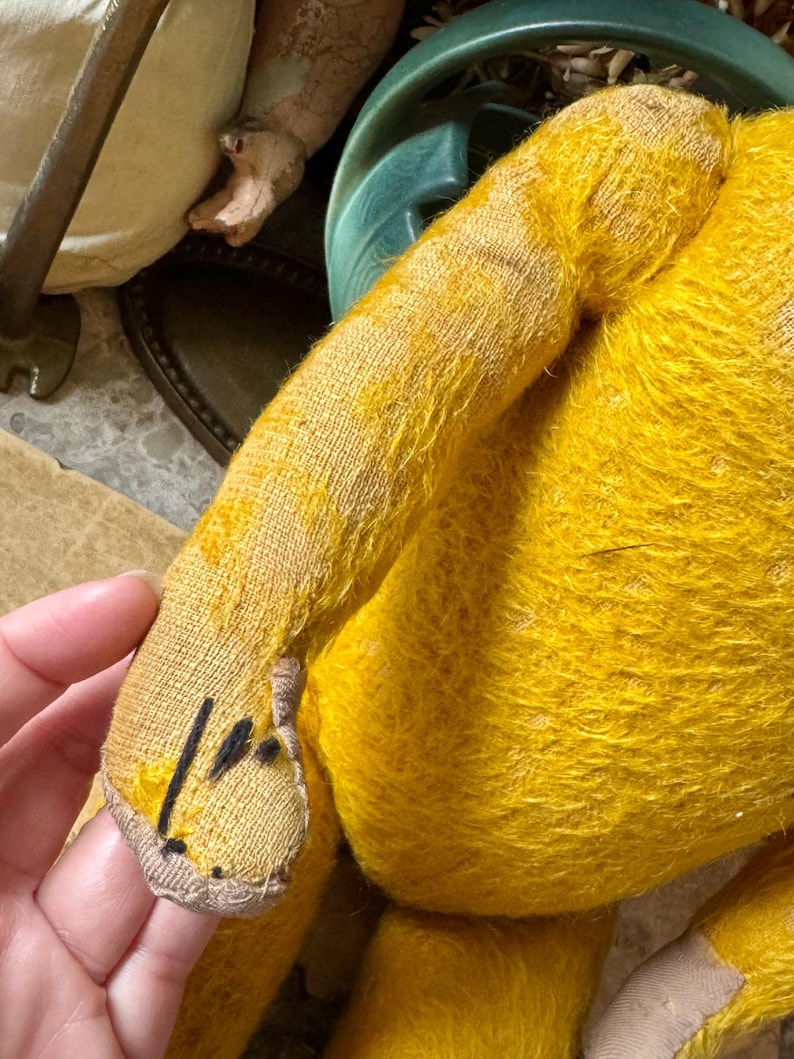 May include: Close-up of a vintage yellow teddy bear. The bear's arm is in focus, showing the textured fabric and stitching details. The bear's fur is a vibrant yellow, with a slightly worn appearance. The bear's paw has black markings.