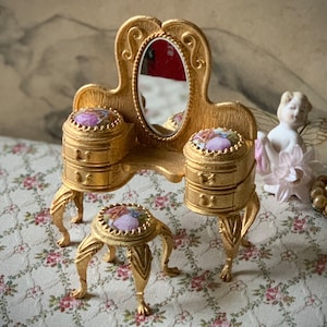 May include: A miniature gold vanity set with a mirror, two drawers, and a stool. The vanity and stool are decorated with floral designs.