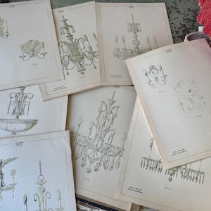 May include: A collection of off-white paper sheets featuring detailed black ink illustrations of various chandeliers and wall sconces. Each page displays technical drawings of lighting fixtures with small printed text labels identifying the specific designs.