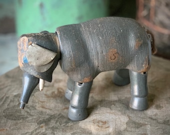 May include: A vintage wooden elephant toy, painted gray with visible wood grain and wear. The elephant has articulated legs and a trunk, with a small number "5" marked on its side. The ears are made of a light-colored material.