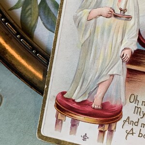 Pode incluir: Postal vintage com uma crian&ccedil;a em camisola branca segurando uma vela. A crian&ccedil;a est&aacute; em p&eacute; em um pequeno banquinho vermelho. O postal tem uma borda dourada, com o texto "Oh my..." vis&iacute;vel.