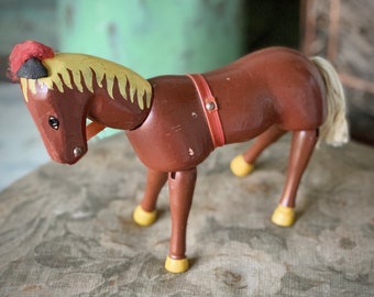 May include: A vintage wooden toy horse in shades of brown, with a yellow mane and tail. The horse has a red harness and yellow hooves. The toy is likely from the mid-20th century, showcasing a classic design.