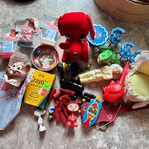 May include: A collection of vintage toys and trinkets including a red plush dog, a mouse hand puppet, a box of 24 Crayola crayons, a cat-themed tin, a small white figurine, various plastic pencil sharpeners, a red fish, and a miniature chair.