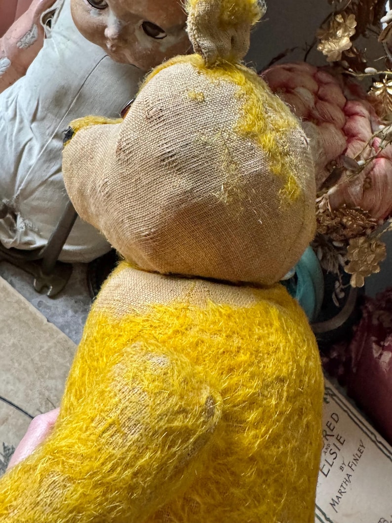 May include: A vintage teddy bear with a yellow fuzzy body and a tan head. The bear's head is made of a burlap-like material. The bear is missing an eye. The bear is a classic toy.