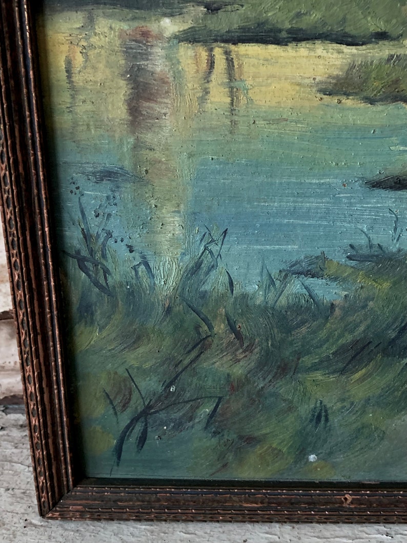 Peut inclure: Une peinture encadr&eacute;e repr&eacute;sentant une sc&egrave;ne de paysage avec une rivi&egrave;re et des arbres. La peinture est r&eacute;alis&eacute;e dans une palette de couleurs douces, des verts, des bleus et des jaunes. Les coups de pinceau sont visibles et donnent &agrave; la peinture un aspect textur&eacute;.