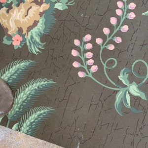 May include: A vintage wallpaper with a floral pattern. The wallpaper features pink flowers, green leaves, and a brown background. The wallpaper is cracked and worn, giving it a vintage look.
