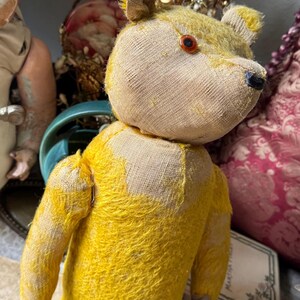 May include: A vintage teddy bear with a yellow body and a tan head. The bear has a button eye and a black nose. The bear's fur is worn, giving it a well-loved appearance. The bear is a classic toy.