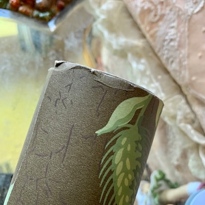 May include: Close-up of a roll of brown and green wallpaper with a leaf pattern. The wallpaper has a textured surface.