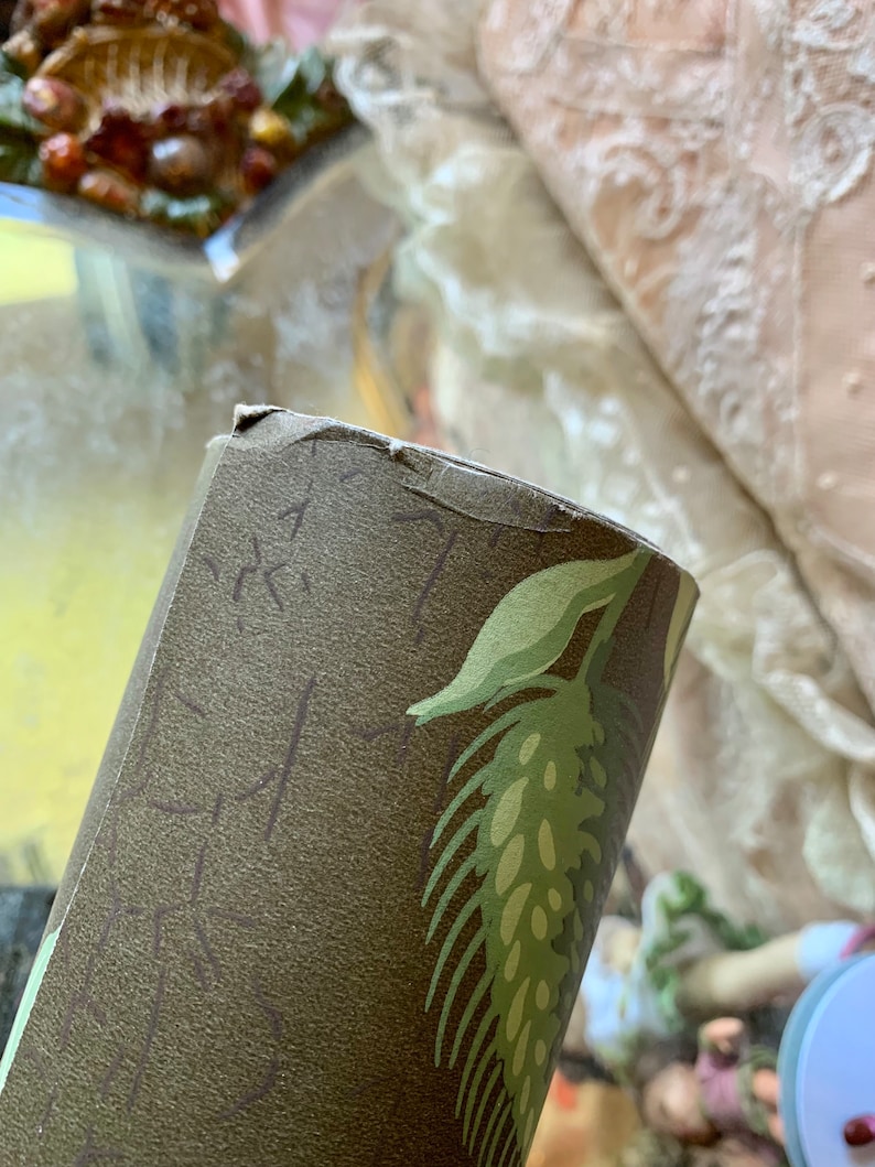 May include: Close-up of a roll of brown and green wallpaper with a leaf pattern. The wallpaper has a textured surface.