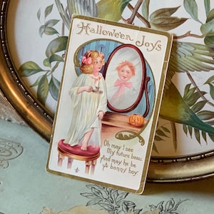 Pode incluir: Postal vintage de Halloween com uma menina de camisola segurando uma vela, olhando para um espelho. O espelho reflete um menino. O cart&atilde;o tem o texto "Halloween Joys" e um poema.