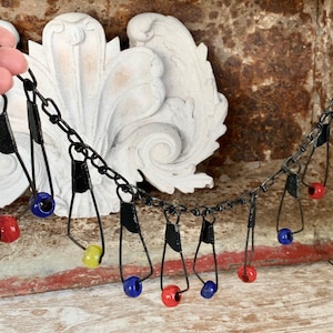 May include: A black chain necklace with metal pendants and colorful glass beads. The beads are red, blue, and yellow.