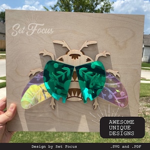 Puede incluir: Un recorte de madera de un escarabajo con alas iridiscentes. El escarabajo lleva gafas de sol verdes con un patrón floral. El fondo es un panel de madera claro con el texto "Set Focus" y "AWESOME UNIQUE DESIGNS .SVG and .PDF" impreso en él.