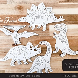 May include: Five white dinosaur skeleton puzzle pieces on a wooden background. The text "Set Focus" and "5 Dinosaur Puzzle" are visible. The text ".SVG and .PDF" is also visible.