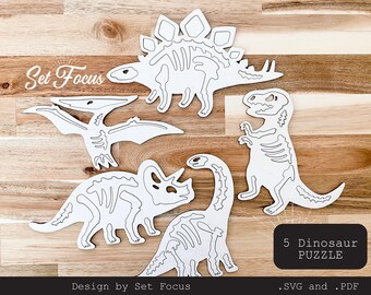 May include: Five white dinosaur skeleton puzzle pieces on a wood background. The text "Set Focus" and "5 Dinosaur Puzzle" are visible. The text ".SVG and .PDF" is also visible.