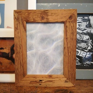 May include: A rustic wooden picture frame with a light blue and white abstract image inside. The frame is made of natural wood with knots and grain showing.