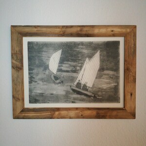 May include: A framed black and white print of a seascape with two sailboats. The sailboats are in the water and there are people on board. The print is in a rustic wooden frame.