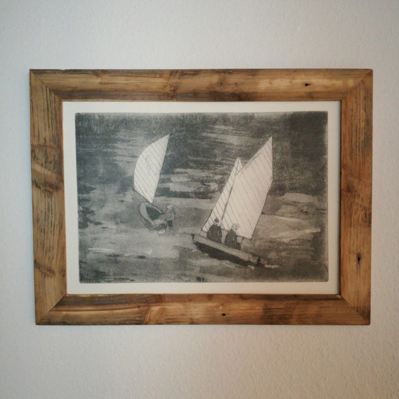 May include: A framed black and white print of a seascape with two sailboats. The sailboats are in the water and there are people on board. The print is in a rustic wooden frame.