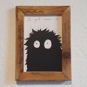 Könnte beinhalten: Gerahmtes Kunstwerk mit einer skurrilen schwarzen Kreatur mit großen weißen Augen und stacheligem Haar. Das Kunstwerk befindet sich in einem rustikalen Holzrahmen und enthält handgeschriebenen Text oben.